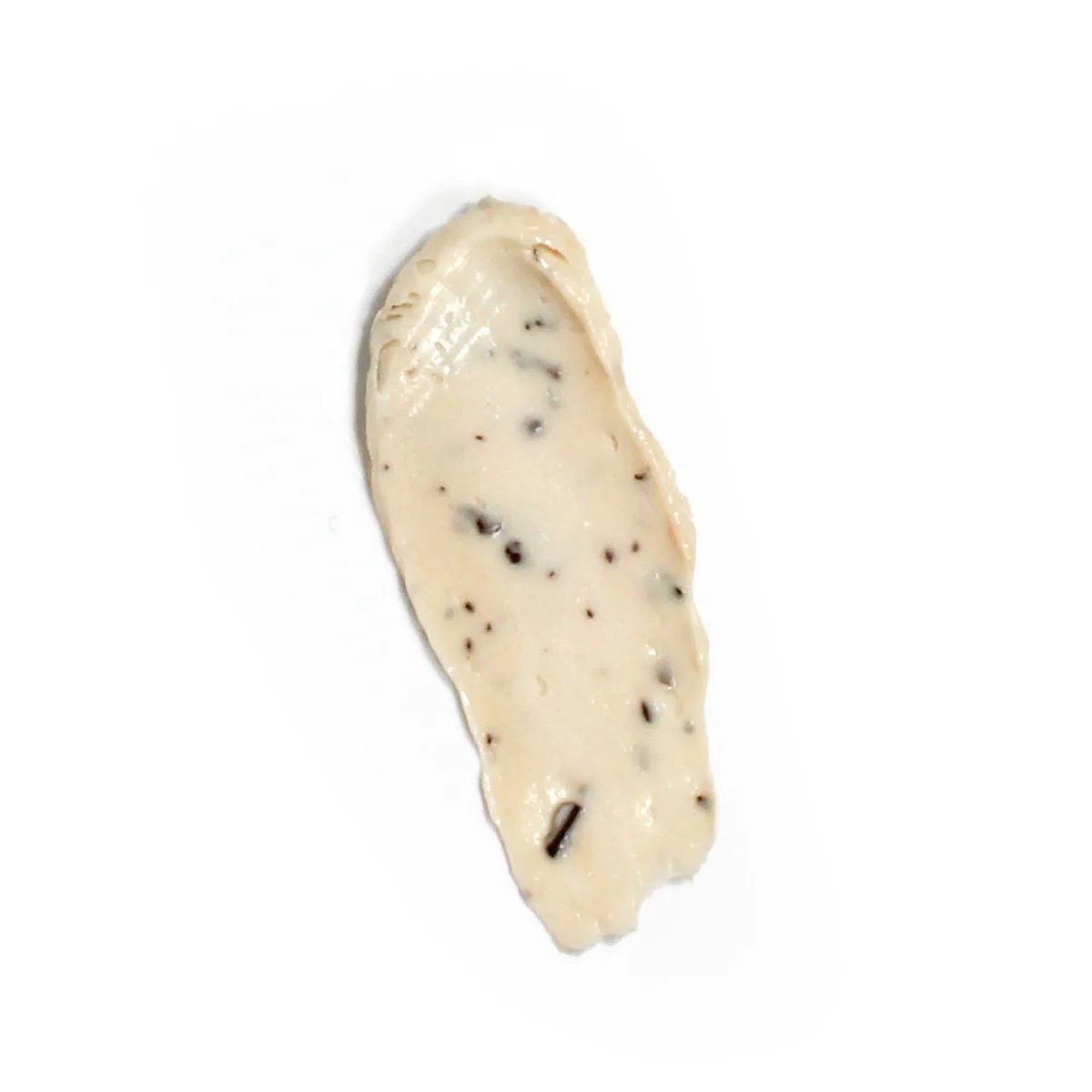 Nahaufnahme einer beigen Gesichtspeeling-Textur mit dunklen Partikeln auf weißem Hintergrund.