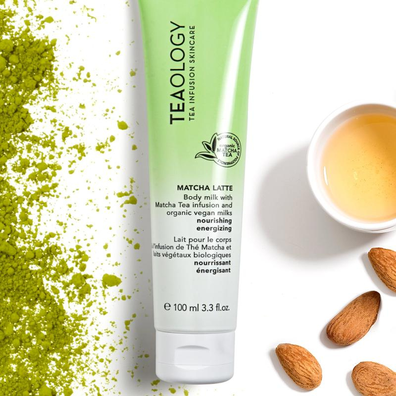 TEAOLOGY Matcha Latte Body Milk 100ml Tube, umgeben von Matcha-Pulver, Mandeln und einer Tasse Tee.