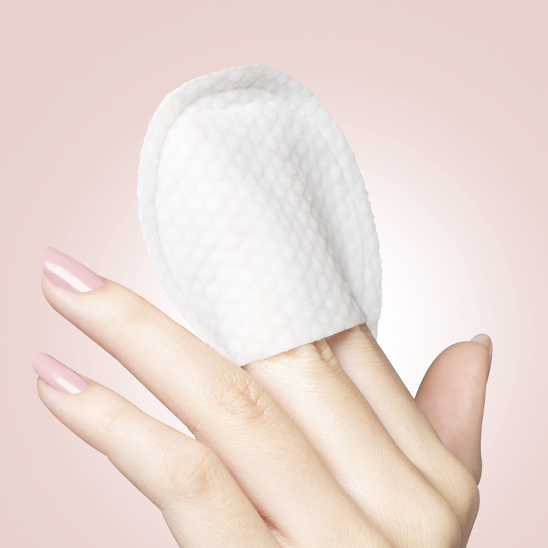 Hand mit rosa lackierten Nägeln hält eine weiße, strukturierte Gesichtsmaske vor einem rosa Hintergrund.