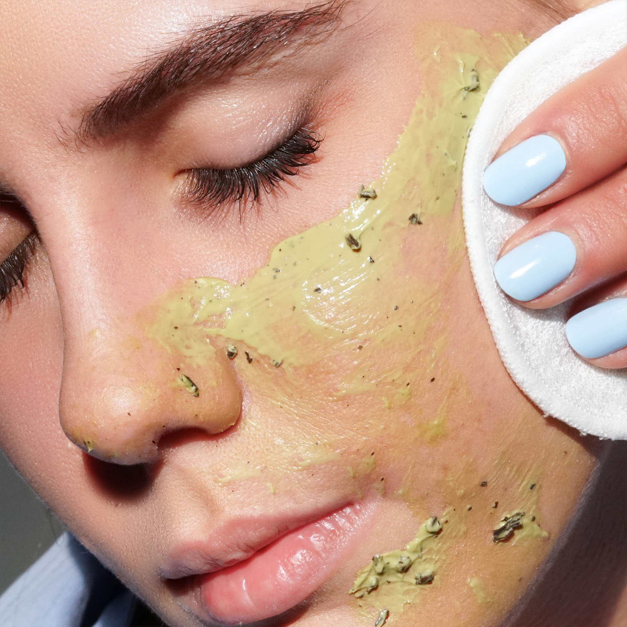 Nahaufnahme einer Frau, die eine goldene Matcha-Gesichtsmaske mit einem Wattepad aufträgt.