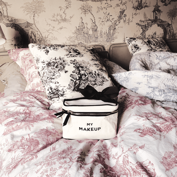 Make-up-Tasche auf einem Bett mit gemusterten Kissen und Decken.