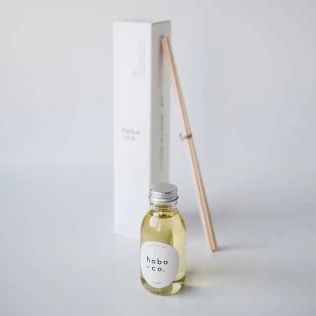 Kleine Flasche mit Duftöl von hobo & co. und Holzstäbchen vor weißem Hintergrund.